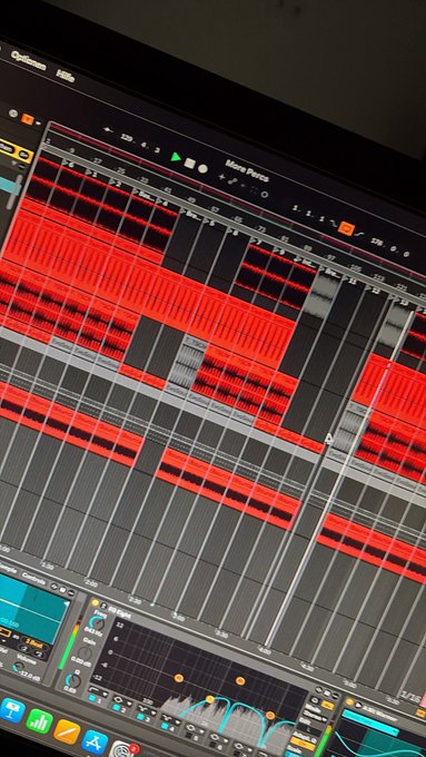 A screen displays a digital audio workstation (DAW) interface with a timeline showing multiple red audio tracks, with various editing tools and panels visible at the top and bottom.