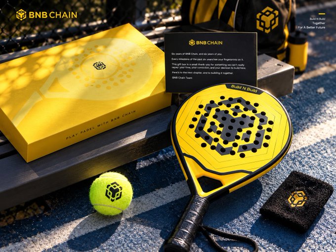 A promotional image for BNB Chain featuring a yellow and black padel racket, tennis ball, branded box, and wristband on a tennis court, with text 'Play Padel with BNB Chain' and 'Build N Build Together For A Better Future'.
