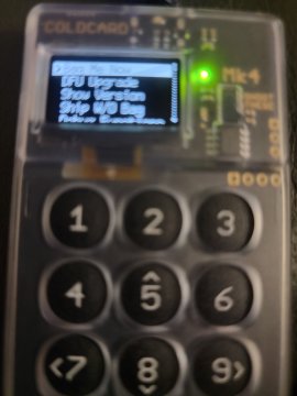 Close-up of a Coldcard Mk4 hardware wallet displaying a menu with options including 'Upgrade', 'Secure Element', 'BBQ USB Logo', and 'Version: v3.1.3', above a numeric keypad.