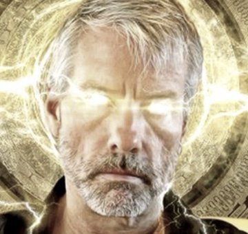 The image features a man with a white beard standing against an orange background, which appears to be a clock or a sunburst pattern. There's also a lightning bolt depicted near the center of the scene. 

The caption for this image is "BREAKING: MICHAEL SAYLOR ANNOUNCES STRATEGY WILL PAY 11.5% ANNUAL #BITCOIN DIVIDENDS IN JUNE SAYLOR IS ABOUT TO BUY MASSIVELY HERE WE GO". The man in the picture has a serious expression, which adds to the overall atmosphere of the image and makes it more relevant to the post.