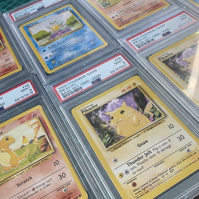 A collection of graded 1999 Pokemon Game Base Set cards, including PSA-graded Pikachu, Charmander, and Squirtle cards in protective slabs, displayed on a green cutting mat.