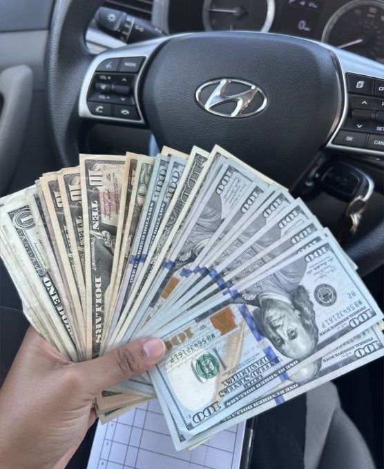A hand fans out a thick stack of $100 bills in front of a Hyundai steering wheel, visually reinforcing the post's message that financial abundance is within reach and ready to pursue those who claim it.