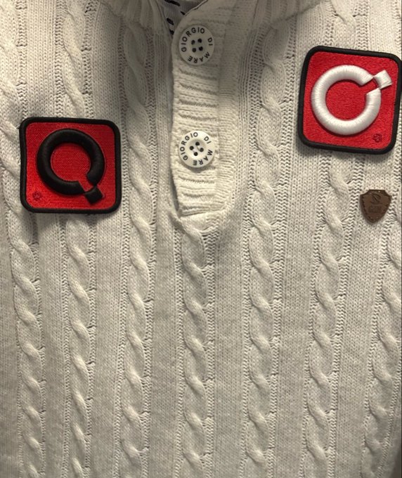 A close-up of a cream cable-knit cardigan shows red-and-black square letter patches, including a black “Q” and white “G,” along with small round buttons labeled “GIORGIO ARMANI.”