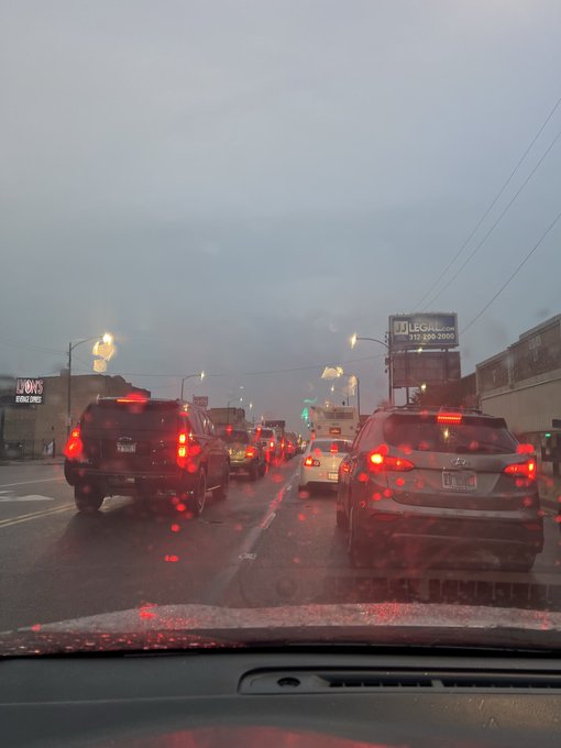 A rainy drive through city traffic shows red brake lights illuminating the wet windshield, with visible signs for "U-Haul" and "LECH" with phone number "317-800-2000".