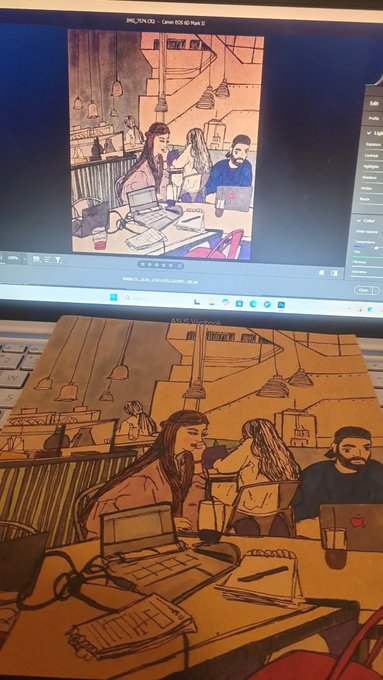A photograph showing a digital illustration on a laptop screen of people working at a café with laptops, with a corresponding printed version of the same artwork laid on the laptop keyboard below it.