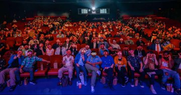 A group photo of attendees seated in a cinema or auditorium, likely at a crypto or tech conference.