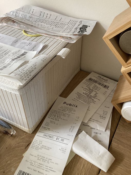 A casual photograph showing several crumpled grocery and retail receipts (Publix, Michaels, Ulta) scattered on a wooden surface next to a woven storage basket.