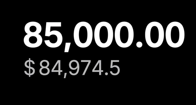 A black screen displays the numbers '85,000.00' in large white text above '$84,974.5' in gray text.