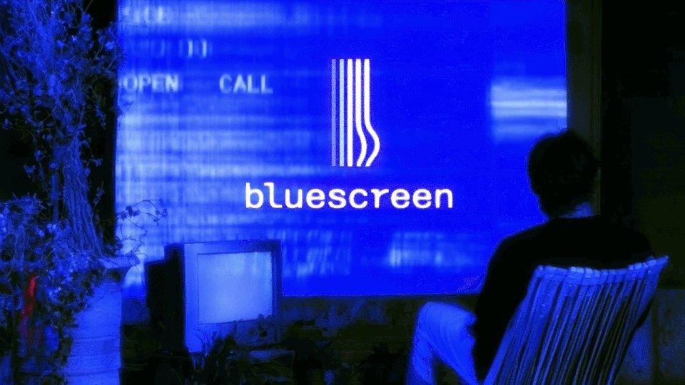 The image shows a person sitting in a chair, watching a television screen that displays the Bluescreen logo. The TV is turned off, with the screen showing the blue letters "BLUESCREEN" prominently displayed. In front of the viewer, there are two potted plants and a vase on a table or shelf.