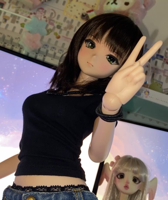 A dark-haired ball-jointed doll in a black crop top flashes a peace sign, with a second blonde doll visible behind her, illustrating the playful shift from Milady-style to smaller "chibi" aesthetic that the post teases.