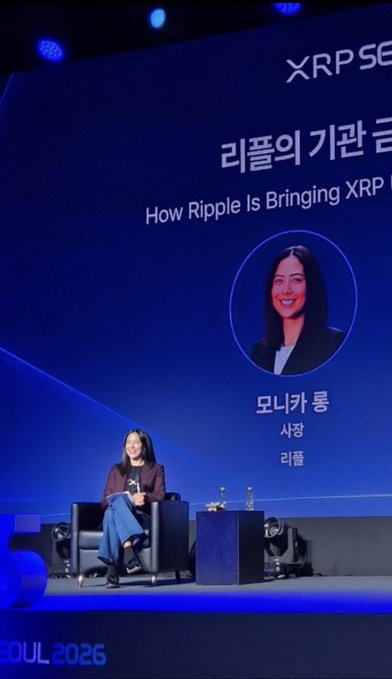 Monica Long, President of Ripple, sits on stage at XRP Seoul 2026, with the screen behind her displaying her name, title ("사장 - 리플"), and the presentation title "How Ripple Is Bringing XRP" alongside Korean text "리플의 기관 글" (institutional). The image captures her delivering the keynote on XRP Ledger's institutional future, aligning with the post's discussion of tokenized RWAs and AI agent transaction projections.