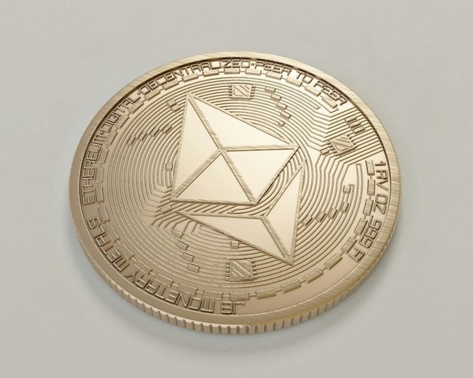 A gold-colored physical Ethereum coin featuring the iconic geometric octahedron logo, 'Ethereum' text around the rim, and 'JAN 02 2019' stamped on the side.