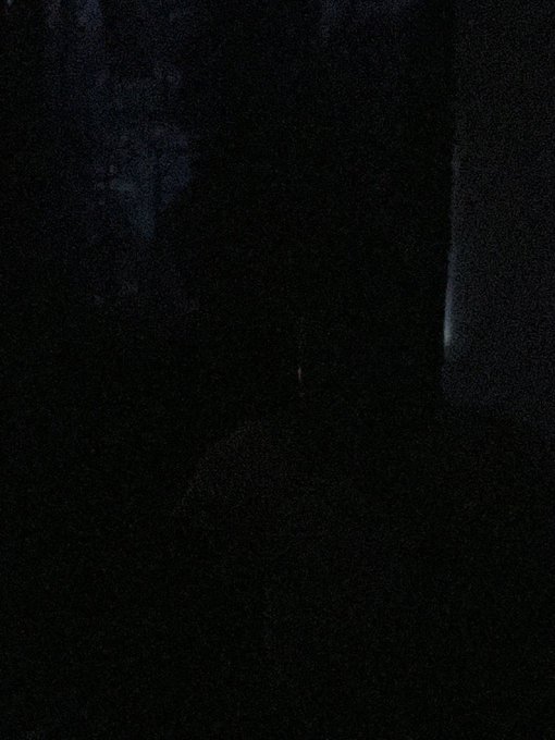 A dark, nearly black image with faint blueish tones and what appears to be a small light or reflection on the right side.