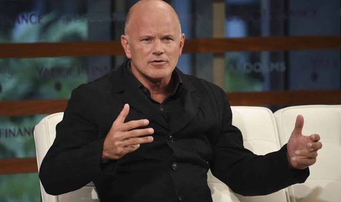 A man in a black suit gesturing with his hands while speaking on a talk show set with 'FINANCE' visible in the background.