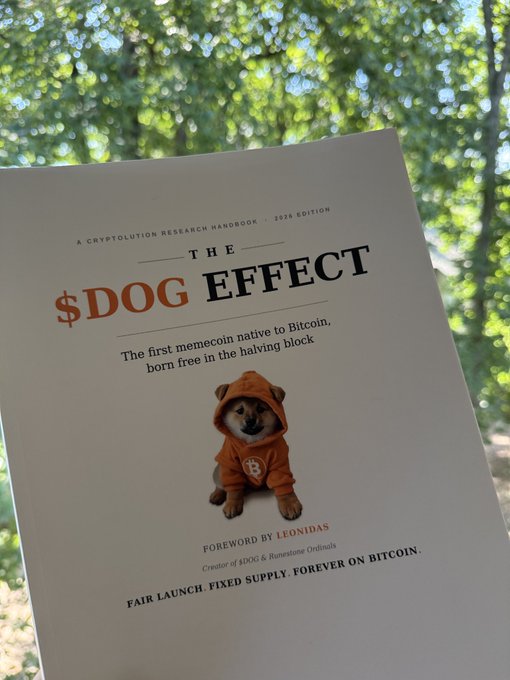 A 2026 edition booklet titled 'THE $DOG EFFECT: A Cryptoevolution Research Handbook,' featuring a Shiba Inu in an orange Bitcoin hoodie on the cover with text reading 'The first memecoin native to Bitcoin, born free in the halving block' and 'Fair Launch. Fixed Supply. Forever on Bitcoin.'