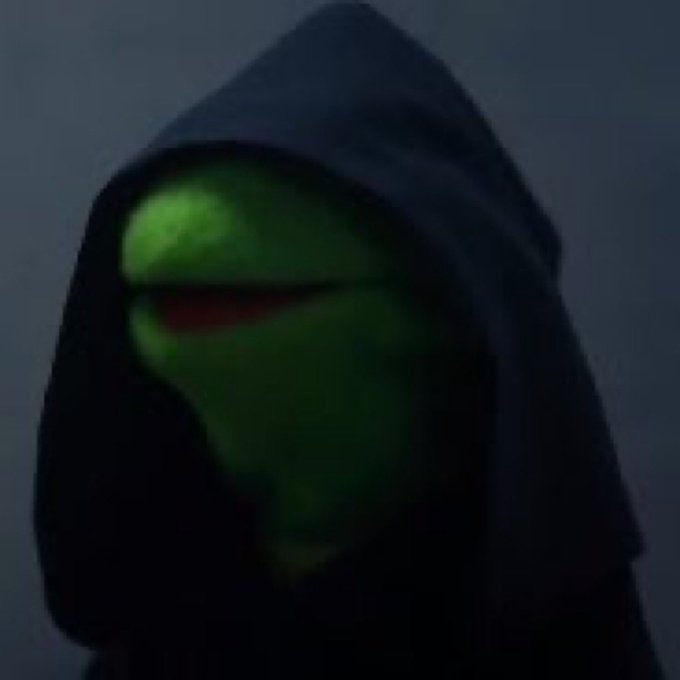 A dark, hooded figure with glowing green skin and red eyes stares menacingly in a dimly lit setting.