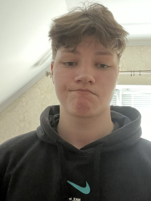 A selfie of a young person wearing a black Nike hoodie, making a pouting expression, in what appears to be a bathroom.