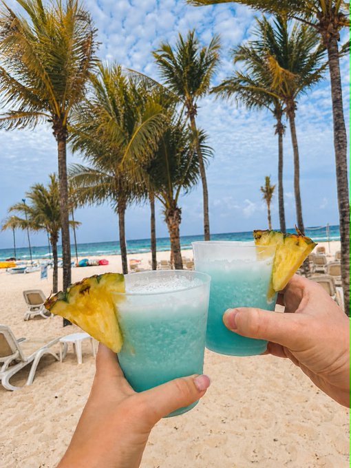 A person holding a glass of pineapple juice with a slice of pineapple on top, while another person holds a similar drink.