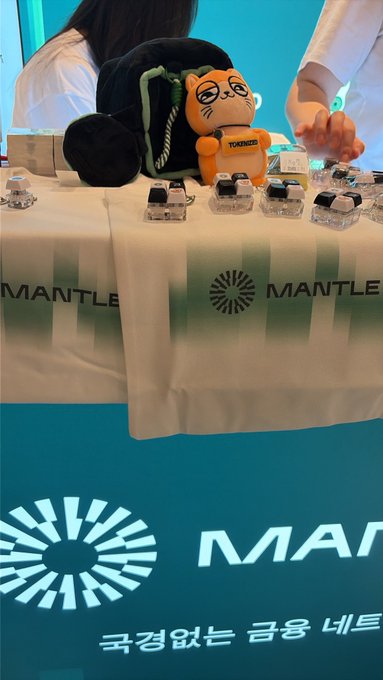A Mantle-branded booth featuring an orange Tokencat plushie and small robotic figurines on display.
