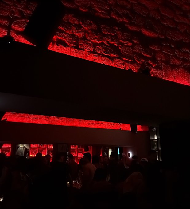 A dimly lit bar or restaurant interior with dramatic red lighting illuminating the textured ceiling, with silhouetted patrons seated below.