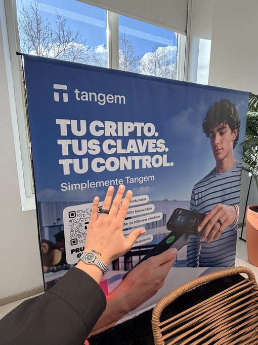 A Tangem crypto advertisement banner in Spanish reading 'TU CRIPTO. TUS CLAVES. TU CONTROL. Simplemente Tangem' with a person's hands holding up in front of it near a window.