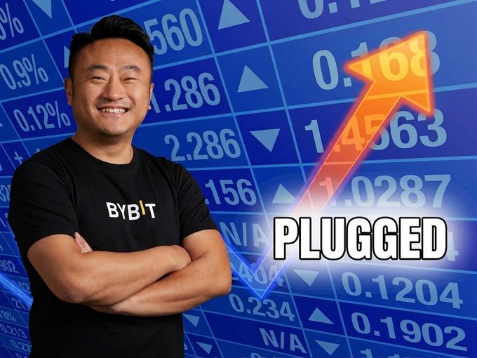 Man wearing a black 'Bybit' t-shirt smiling with arms crossed against a blue background of stock tickers, with an orange upward arrow and the text 'PLUGGED'.