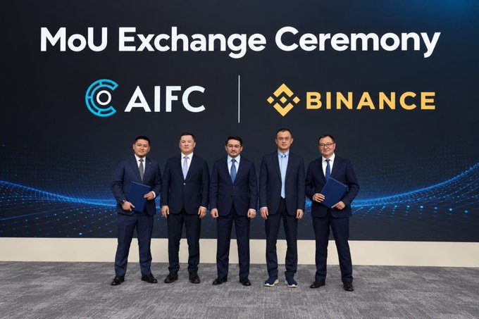 A formal group photo from a 'MoU Exchange Ceremony' between AIFC and Binance, showing five men in business suits standing in a row against a dark blue digital backdrop displaying both company logos.