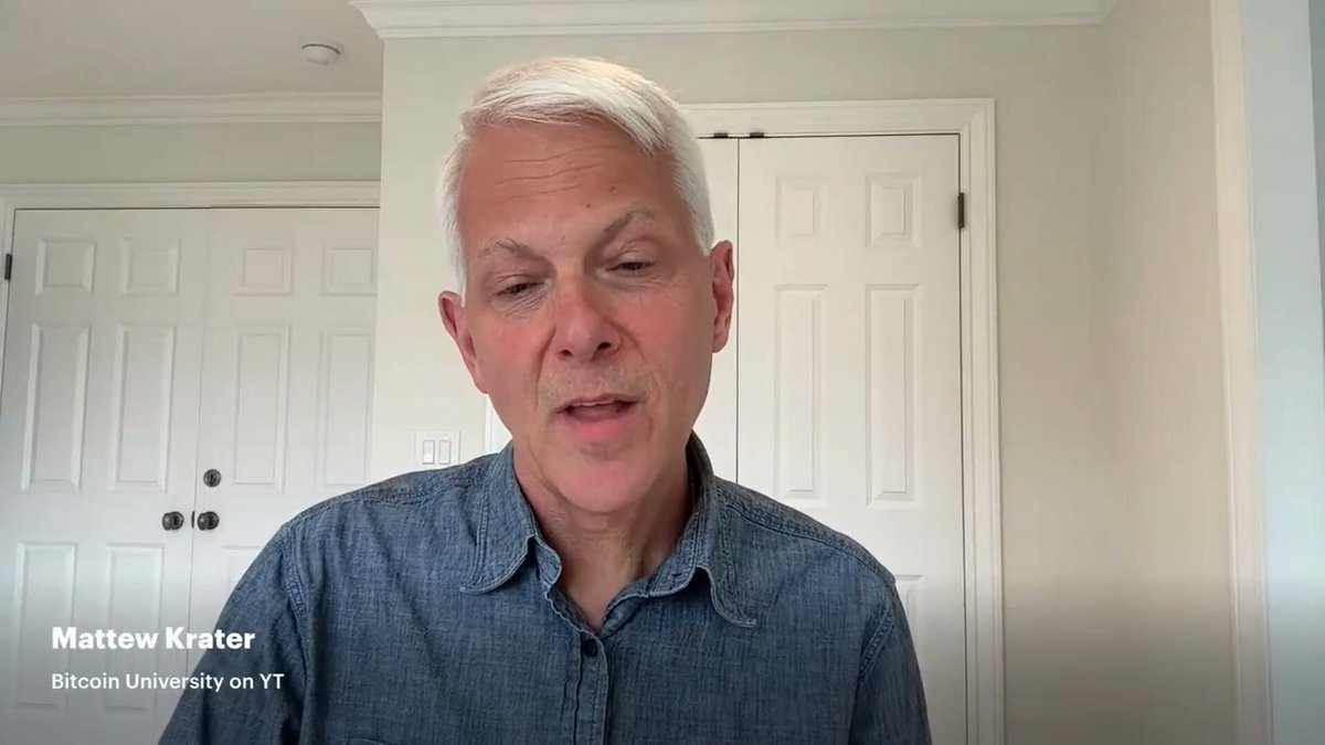 The image shows a man wearing a blue shirt, standing against a white wall with two doors visible behind him. The man appears to be talking or giving a speech, as indicated by his facial expression. The caption of the image reads "Matthew Kratter from Bitcoin University explains why the biggest concern for Bitcoin is mining centralization." This suggests that the man might be discussing the issue of centralized mining in relation to Bitcoin and its potential impact on the cryptocurrency market.