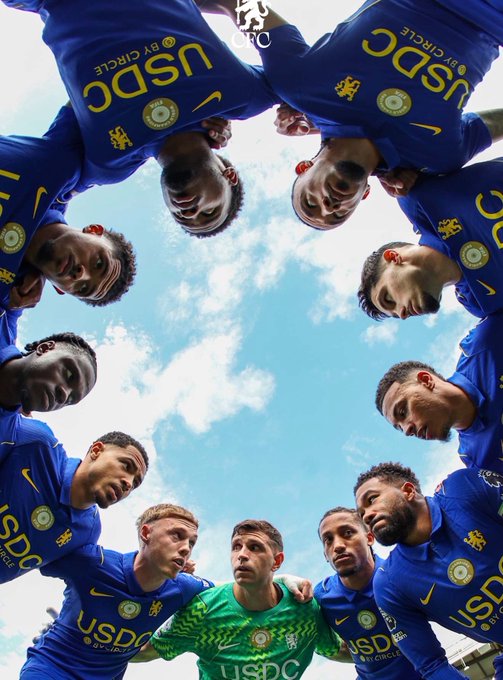 Chelsea FC players huddle together looking down at the camera, wearing jerseys featuring "USDC by Circle" sponsor logos on their chests, highlighting the recent sponsorship partnership between the Premier League club and Circle.
