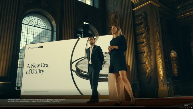 Two presenters stand on a stage in an ornate hall in front of a large screen displaying 'A New Era of Utility' with the Robinhood Chain logo and a note about it being a Layer 2 blockchain.