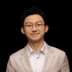 A young East Asian man wearing round glasses, a beige blazer, and a white collared shirt poses against a black background with a slight smile.