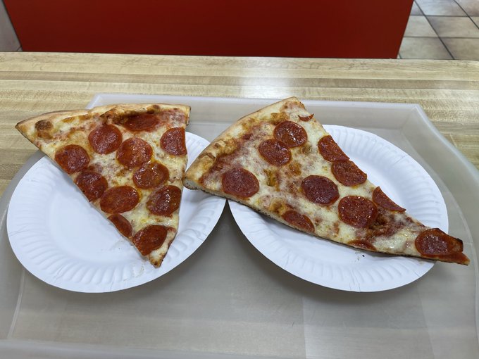 Two slices of pepperoni pizza sit on white paper plates on a light wooden table.