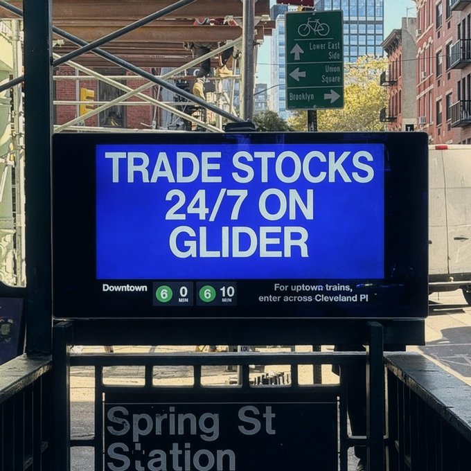 A digital screen at the Spring St Station subway entrance displays a blue advertisement reading "TRADE STOCKS 24/7 ON GLIDER," promoting around-the-clock stock trading, with nearby signage pointing toward the Lower East Side, Union Square, and Brooklyn, visually reinforcing the post's message that Glider lets users trade assets like $NVDA even when traditional markets close for the weekend.