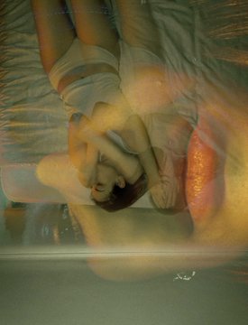 An artistic, blurry double-exposure style image of a person lying down, overlaid with warm orange and yellow light flares.