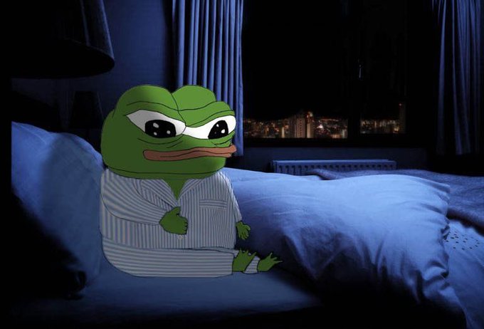 A digitally edited photo of the 'sad Pepe the Frog' meme sitting on a bed in pajamas at night with a city view through the window.
