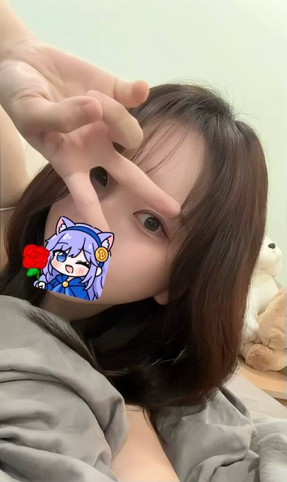 Close-up selfie of a young woman with brown hair making a peace sign, with a small anime cat-girl sticker with a red rose covering part of her face.