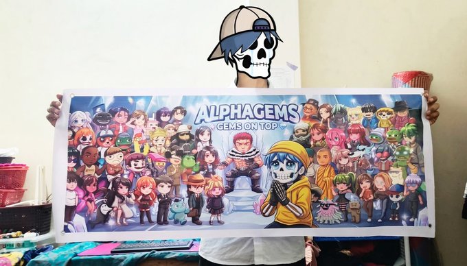 A person wearing a skull-and-cap mask holds up a large banner reading 'ALPHAGEMS - GEMS ON TOP' featuring numerous cartoon-style characters.