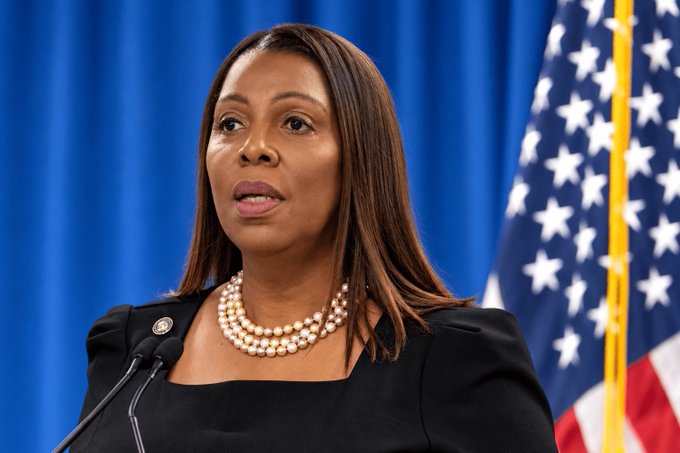 A photograph of New York Attorney General Letitia James speaking at a podium, wearing a black top and pearl necklace, with the American flag visible in the background against a blue curtain.