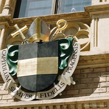 A coat of arms bearing the Latin motto "CAPITULUM SEMPER FRAGENSIS FIDELIS" with a bishop's mitre and crozier is displayed on a building, referencing Czech ecclesiastical heritage. The imagery relates to the news of the Czech Finance Ministry blacklisting Polymarket, as the nation draws on its historical and institutional authority—including religious symbolism—to enforce regulatory actions against unauthorized gambling sites.
