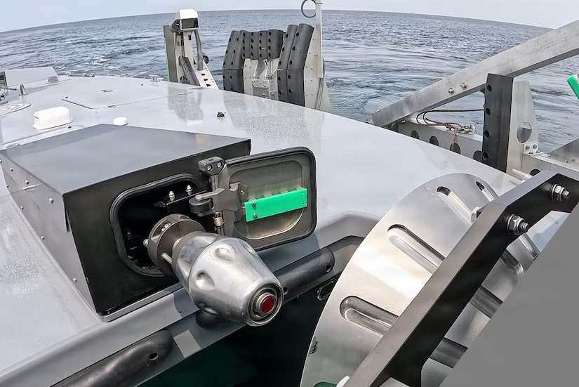 A view from the deck of a boat showing a winch or capstan mechanism mounted on a metal surface, with the open ocean visible in the background.