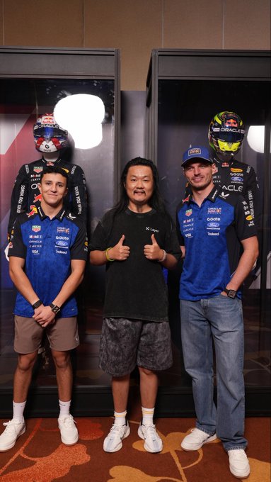 A man wearing a black t-shirt gives two thumbs up while posing for a photo between two F1 drivers in Oracle Red Bull Racing team gear, with racing helmets and gear displayed in display cases behind them.

The post explains that the photo opportunity to meet the F1 racers was arranged through @Godot_gate and @Gate_zh, thanking them for making this special moment possible.