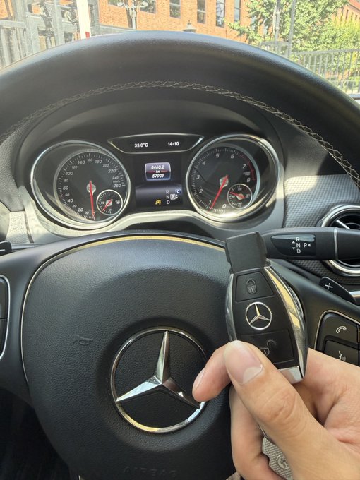 A first-person view inside a Mercedes-Benz vehicle showing the dashboard (44,602 km, 37.9°C) and a hand holding the Mercedes key fob near the steering wheel.