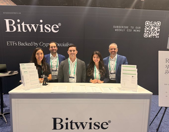 Five Bitwise team members in business attire stand behind a branded booth featuring the Bitwise logo and the tagline "ETFs Backed by Crypto Specialists," along with a QR code promoting their weekly CIO memo. The scene captures the team engaging with attendees at LPL's Focus 2026 conference, embodying the post's message of building bridges for new investors to access crypto opportunities.