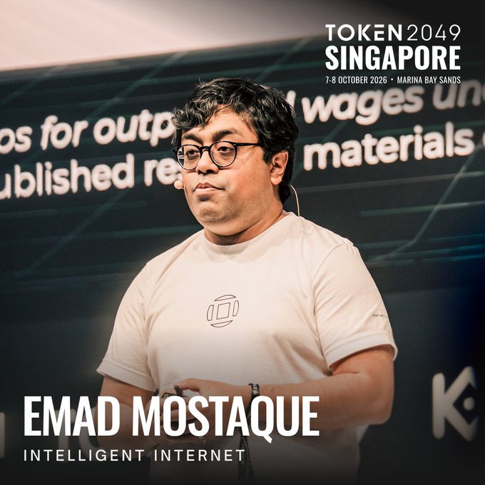 Emad Mostaque, identified by the caption as "INTELLIGENT INTERNET," is shown on stage at TOKEN2049 Singapore (7-8 October 2026, Marina Bay Sands), with the event branding visible in the top right corner. The accompanying text notes his return to the conference as the founder of @ii_posts and former Stability AI chief, where he now advocates for AI ownership.