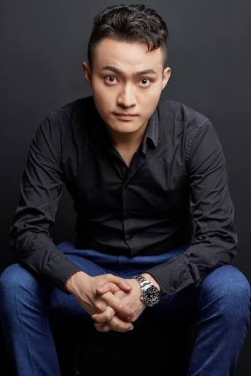 A young man with short dark hair, wearing a black button-down shirt and jeans, sits with hands clasped against a dark background, wearing a wristwatch. The post suggests this is Justin Sun, the entrepreneur behind Peiwo and TRON, whose career began in consumer technology rather than blockchain.
