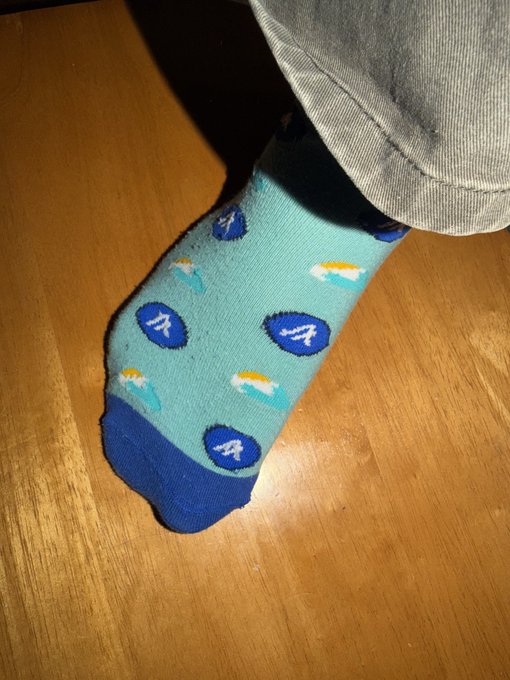 A person's foot wearing a teal sock with blue Auburn University 'A' logos and jet plane designs.