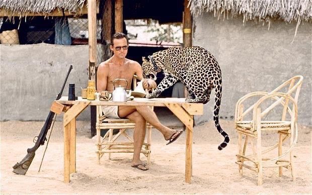 A shirtless man casually shares breakfast with a leopard at a bamboo table, while a rifle leans against it—evoking a relaxed but risky readiness, much like springing into action at the first sign of portfolio gains.