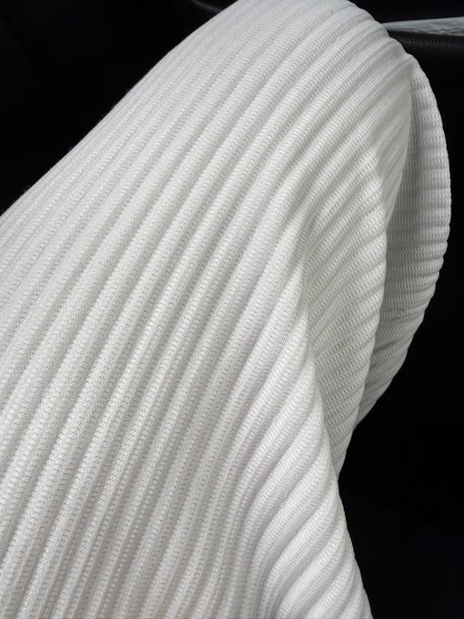 A close-up image showing the distinctive pleated texture of a white Issey Miyake garment, with its signature accordion-like folds prominently displayed. The post references the brand after the author encountered a fellow admirer recognizing their Issey Miyake clothing at a Kalshi event.