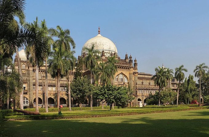 The Chhatrapati Shivaji Maharaj Terminus (formerly Victoria Terminus) in Mumbai, a historic Gothic-style railway building with a prominent dome, surrounded by palm trees and green lawns.