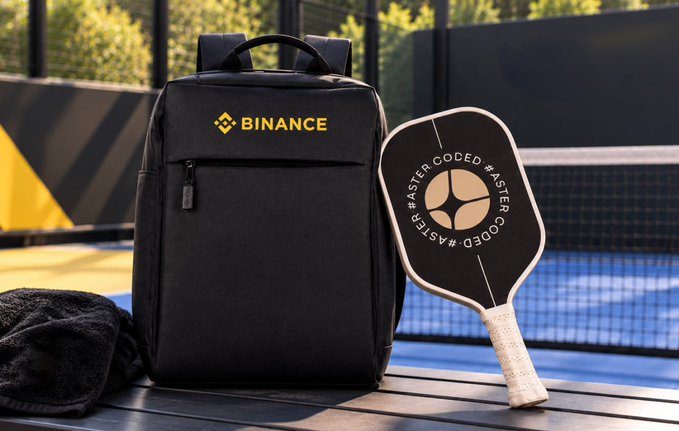 A black backpack with the "BINANCE" logo and a pickleball paddle branded with "#ASTER CODED" sit on a sports court, promoting Binance's live event and inviting viewers to join their Discord for a chance to win branded swag.